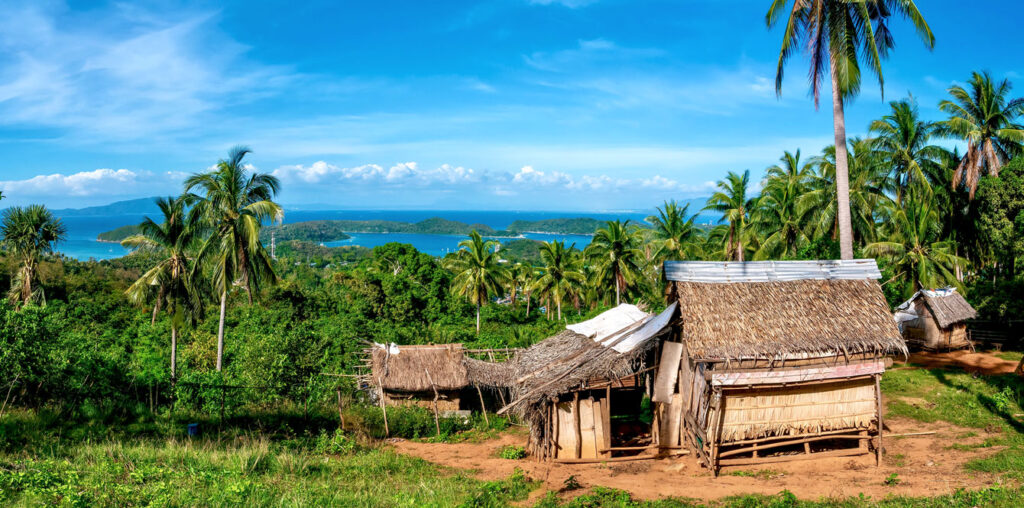 Mindoro island traditional Mangyan house in foreground with palm trees and rainforest, ocean and islands in the distance